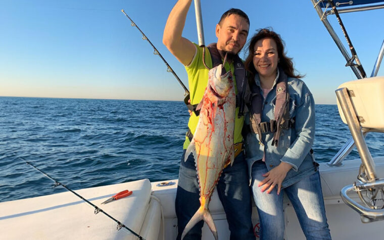Two guests holding a large kingfish aboard the fishing boat off Dubai