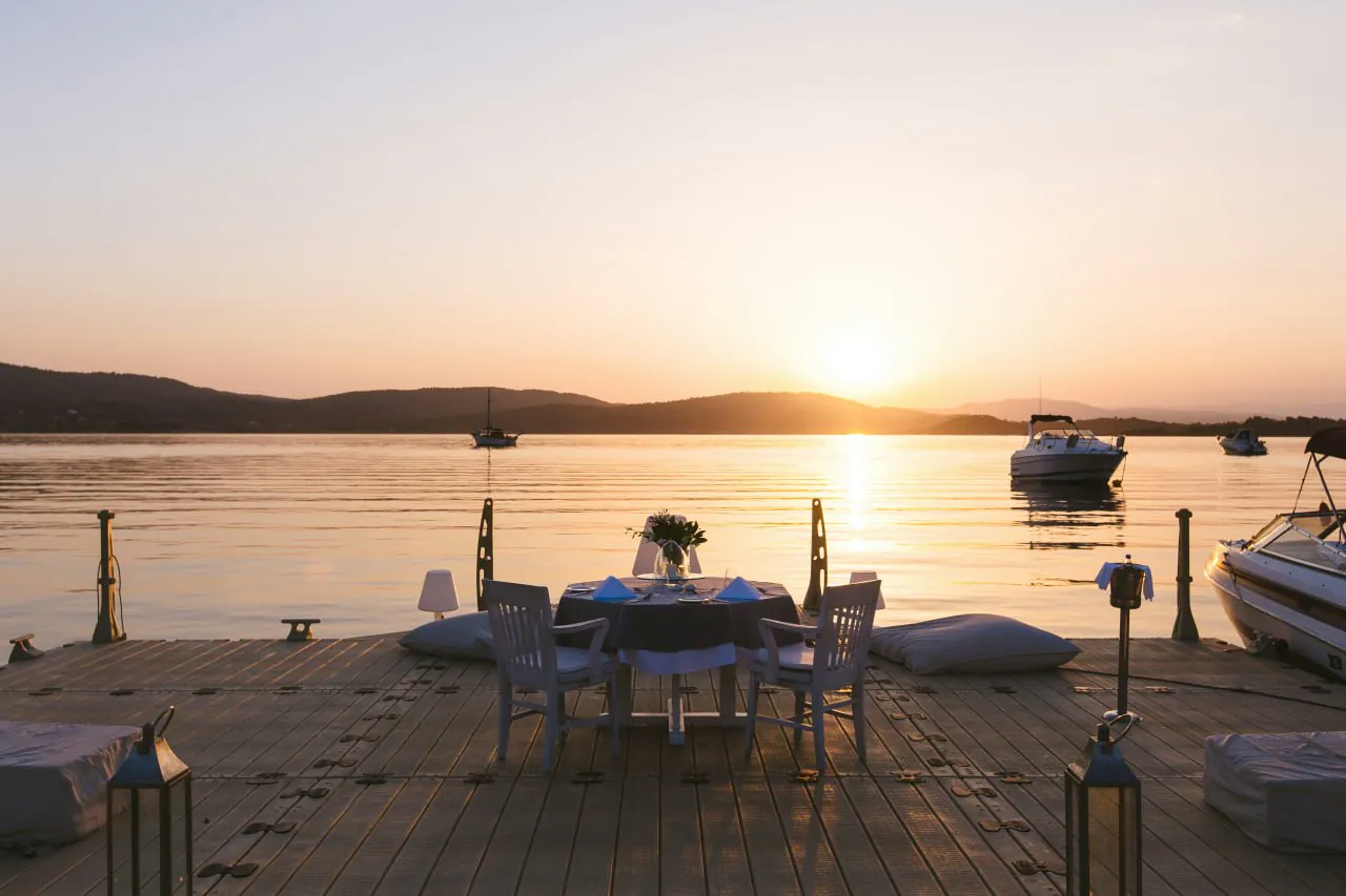Romantic sunset dinner setup on a private dock overlooking the water with mountains beyond