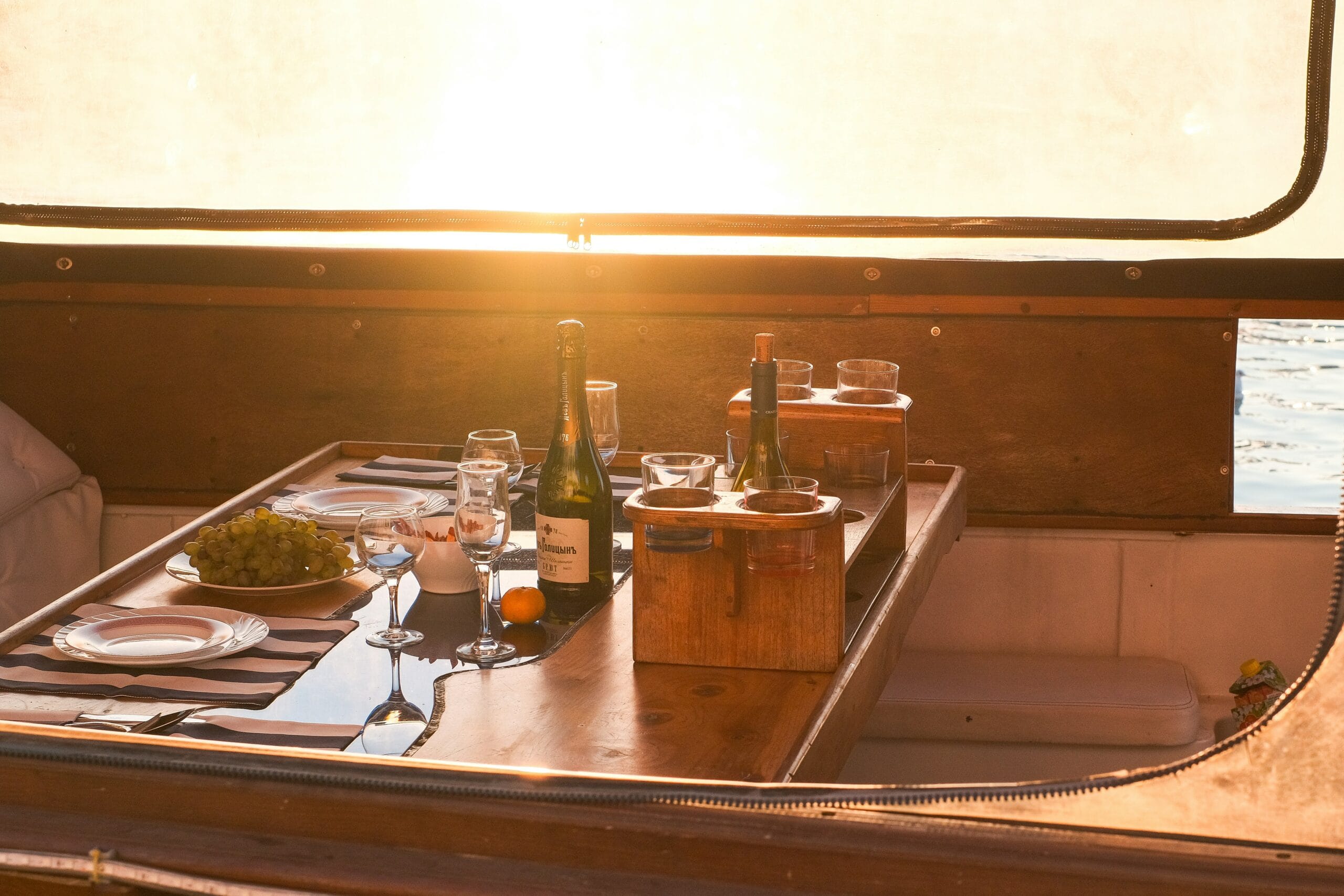 Private yacht dinner table setting — wine, fresh fruit, and tableware with golden sunset light and water views