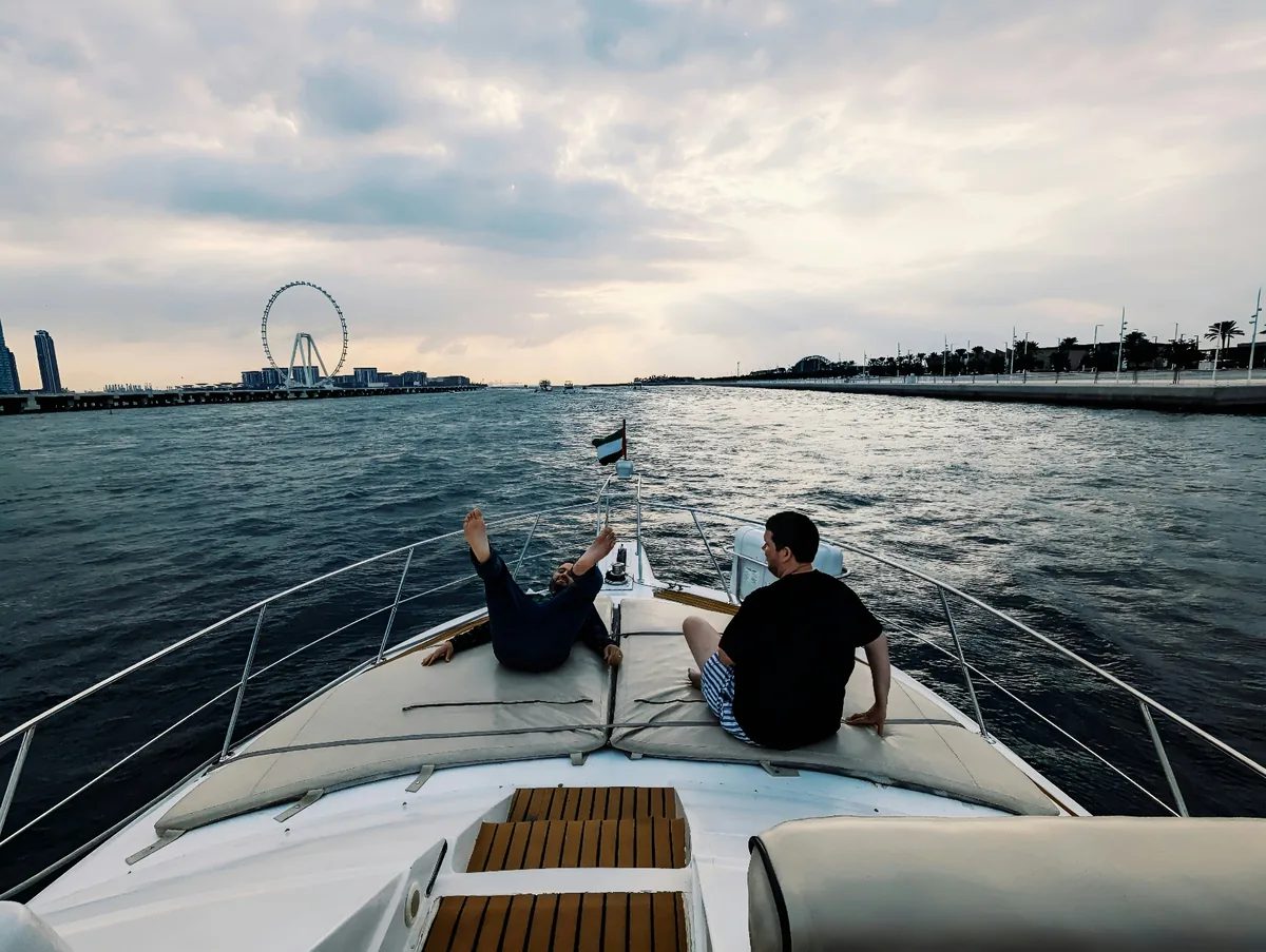 Private yacht charter Dubai — guests relaxing on a private motor yacht deck with Ain Dubai behind